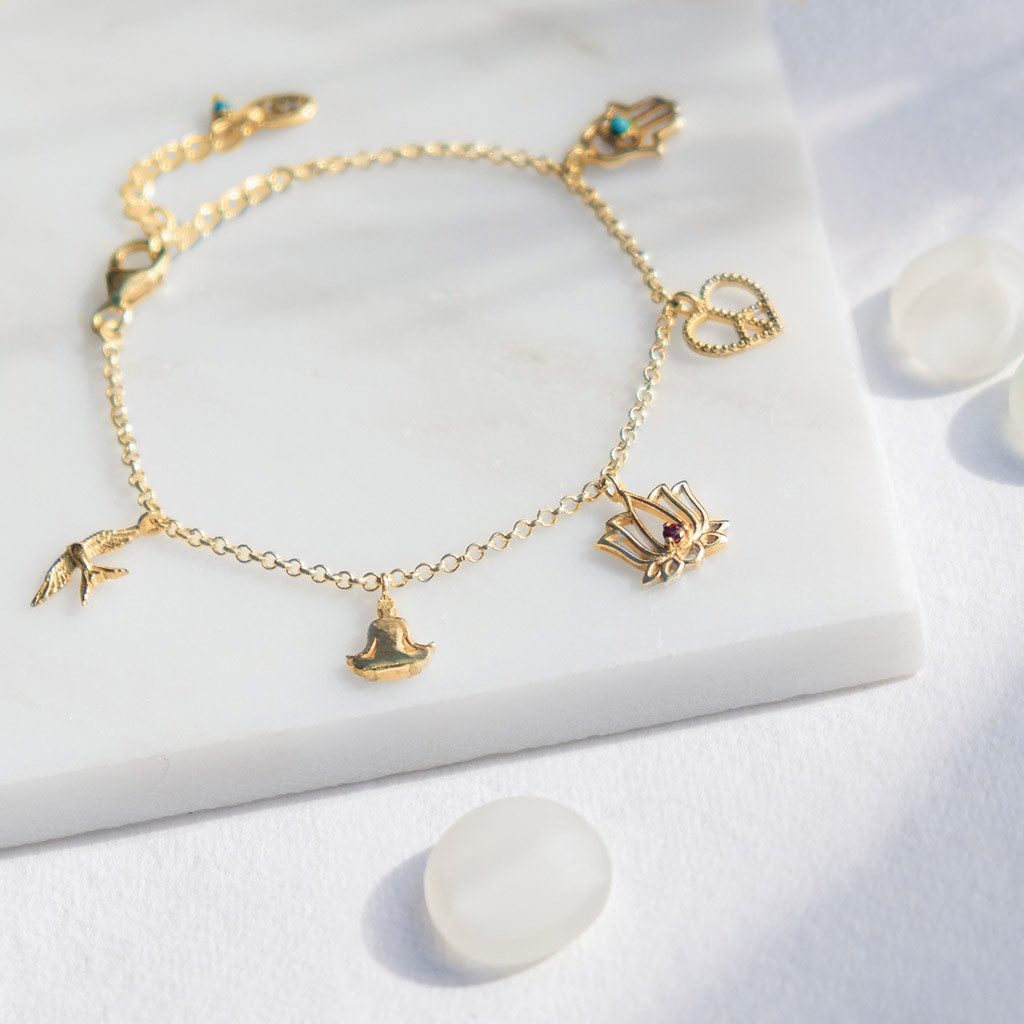 Gold vermeil charm bracelet. There’s a sitting buddha charm, a lotus flower charm with rhodolite garnet, a swallow bird charm to represent freedom, a Hamsa hand charm with turquoise gemstone, and a heart-shaped peace charm.