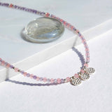 Necklace with pink beads and silver charms on a white surface