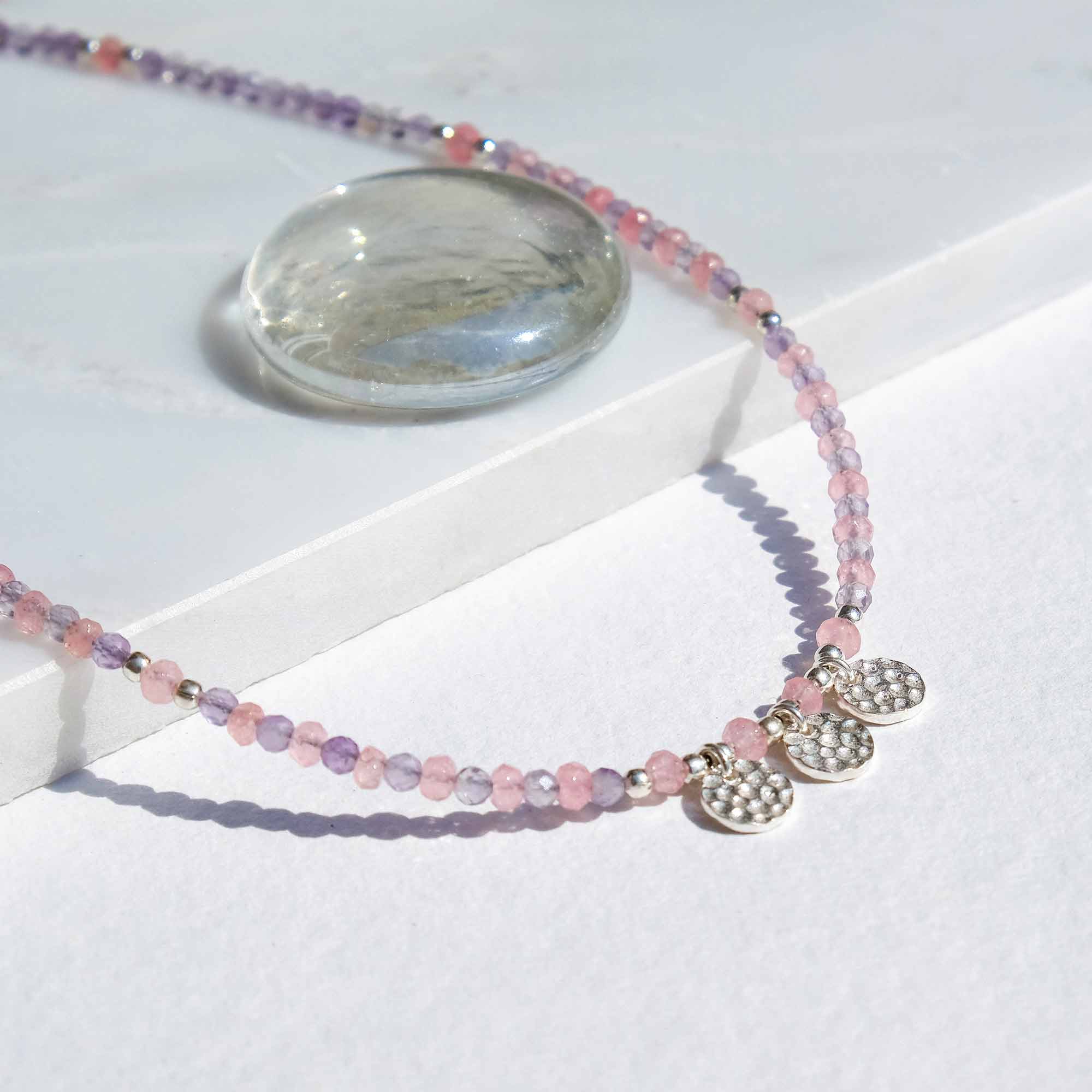 Necklace with pink beads and silver charms on a white surface