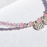 Beaded bracelet with pink and purple beads and a silver charm on a white background