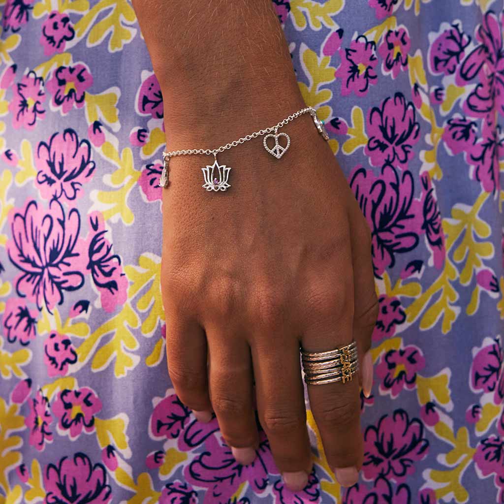 Hand wearing a sterling silver bracelet  featuring sitting buddha charm, a lotus flower charm with rhodolite garnet, a swallow bird charm to represent freedom, a Hamsa hand charm with turquoise gemstone, and a heart-shaped peace charm